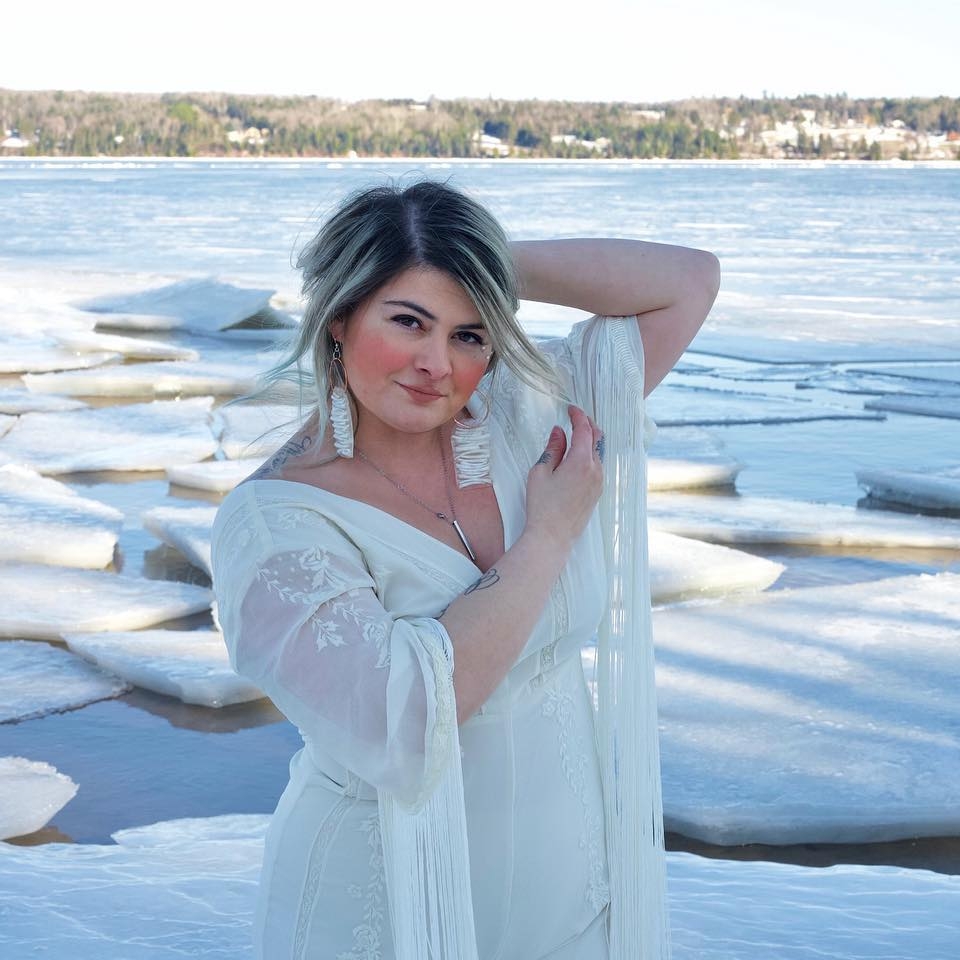Tashina wears a white dress, in the background there is ice cracking over a body of water.